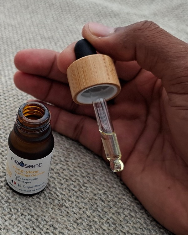 Une main tient la pipette en verre d'un flacon d'huile essentielle d'ylang-ylang